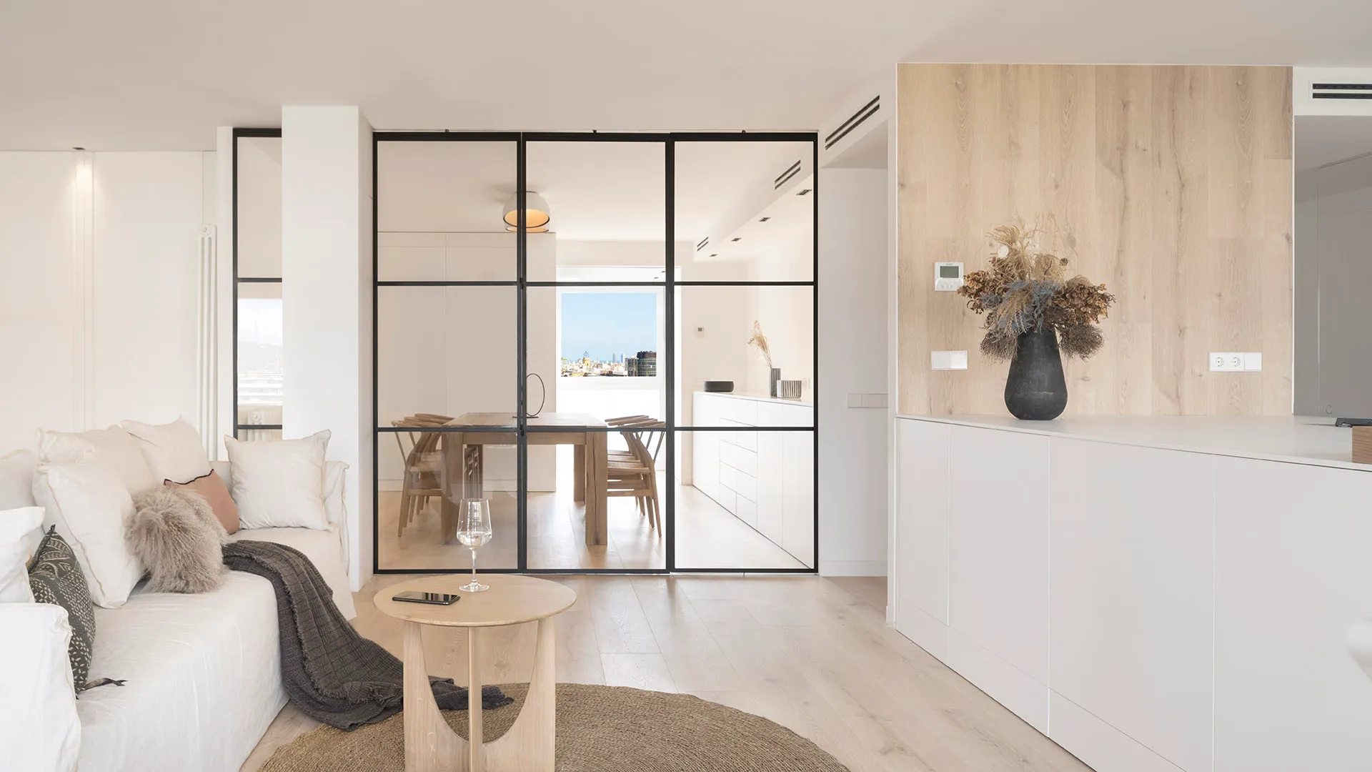 A modern minimalist living room with white furniture, glass walls, and wood accents.