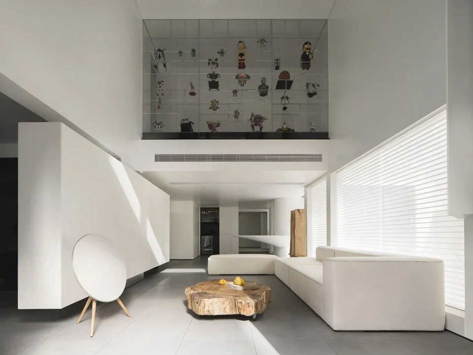 A minimalist living room with a concrete floor, a wooden coffee table, a white sofa, and a white speaker.