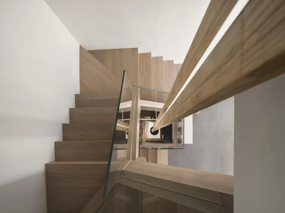 Modern staircase featuring wood stairs with glass railings and a wooden handrail.