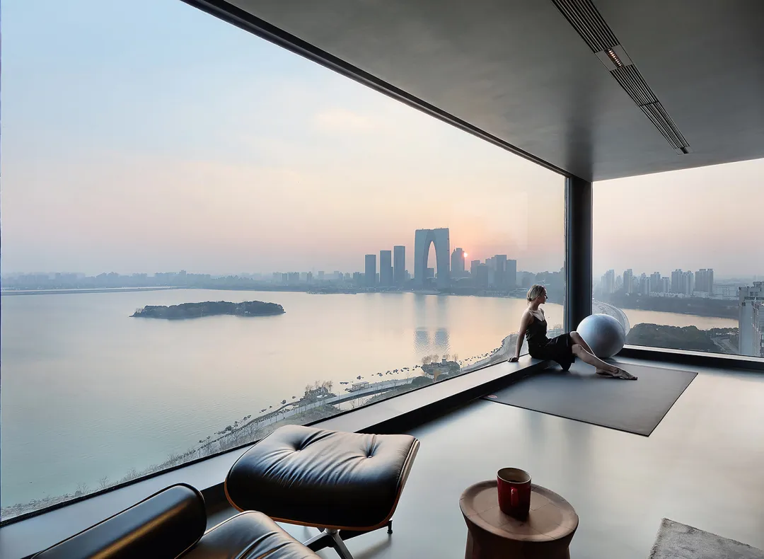 A modern living room overlooking a cityscape through a large glass window at sunset.