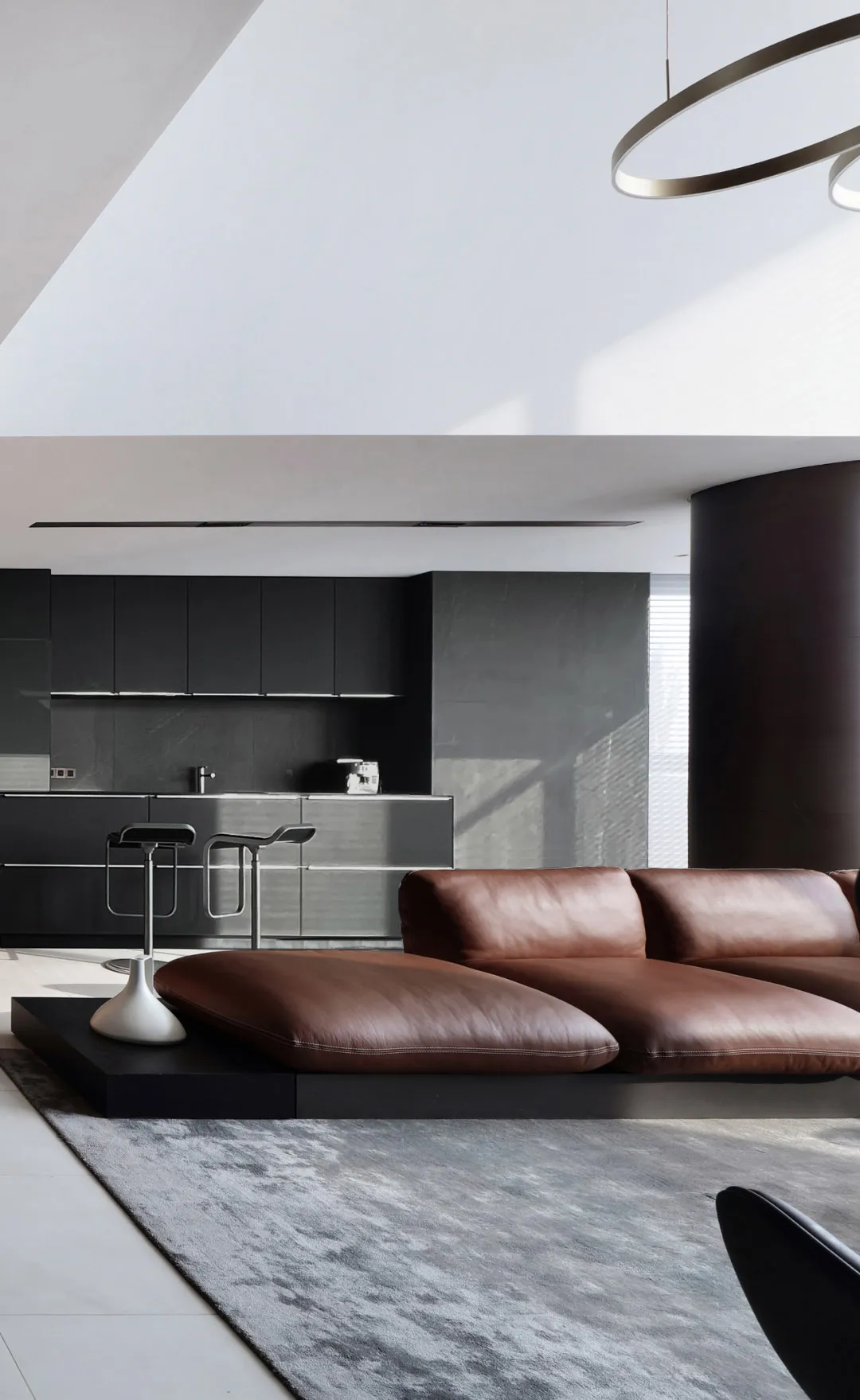 A minimalist living room featuring a brown leather sofa, metal stools, and glass cabinets.