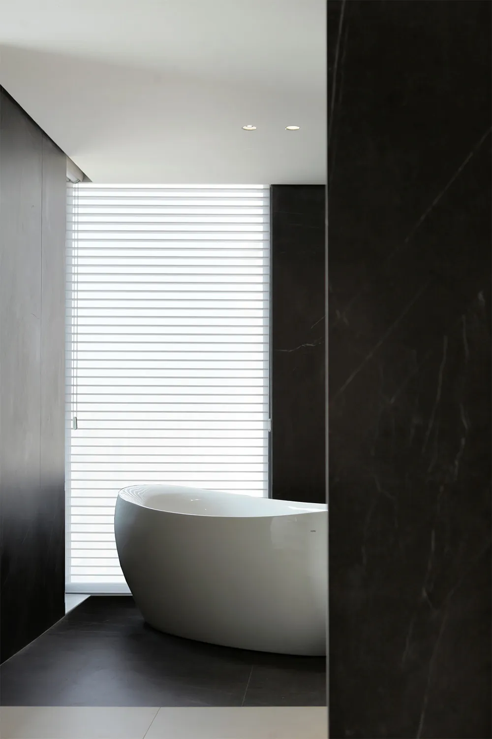 Modern bathroom with white freestanding bathtub against black marble wall and floor.