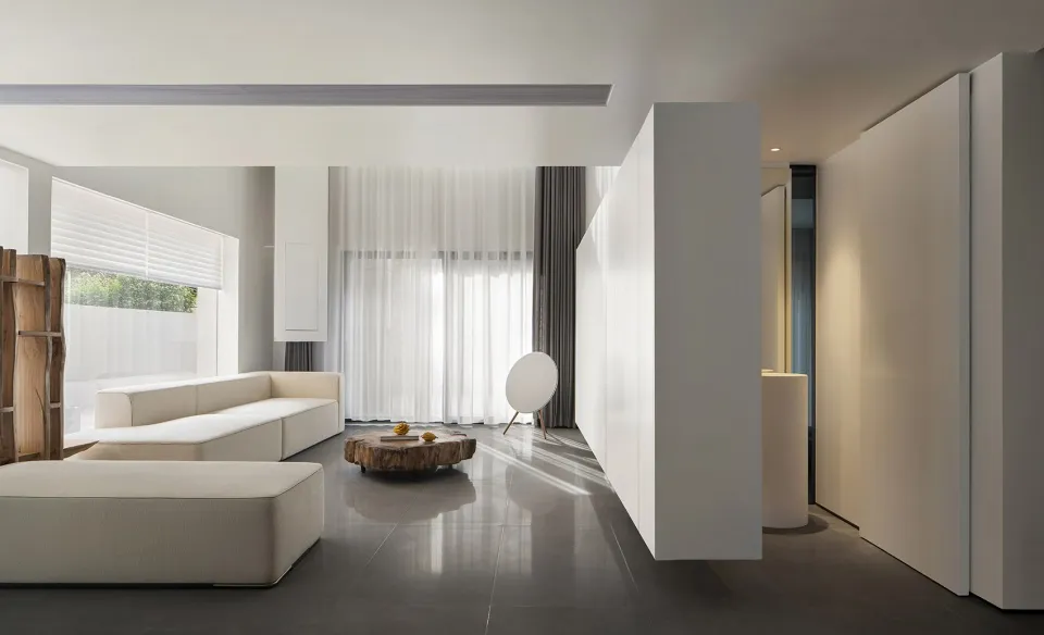 A minimalist living room with white furniture, concrete floor, and large windows.
