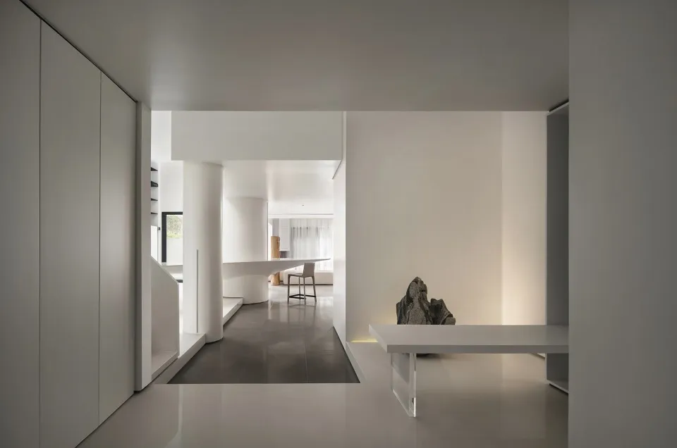 A minimalist interior design in white and black, featuring a concrete floor and walls with a single, modern table.