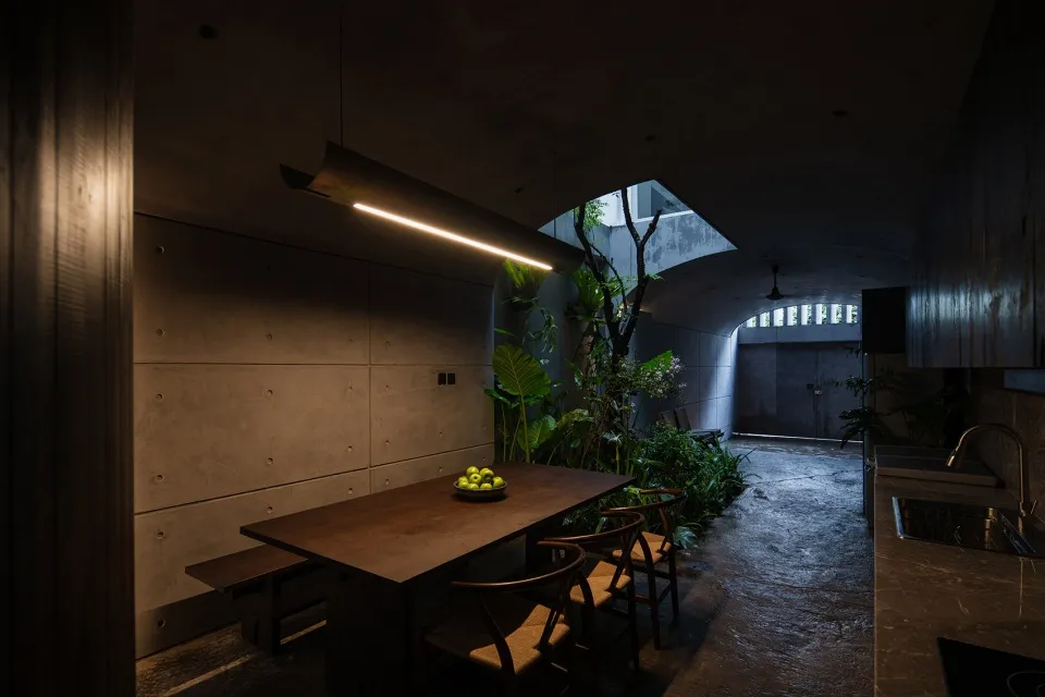 An industrial-themed dining room with a wooden table, chairs, and concrete walls, illuminated by a modern linear light fixtur