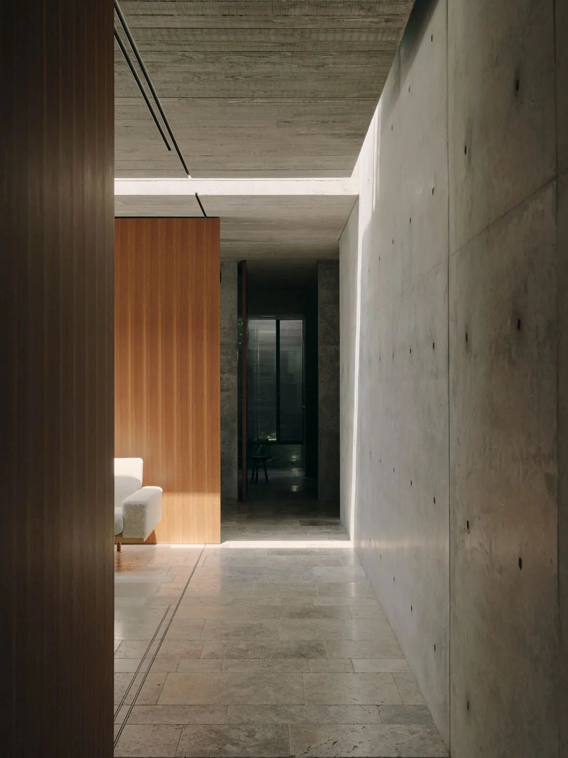 Minimalist design corridor featuring concrete walls and floor, with a wooden partition and a white sofa in the background.
