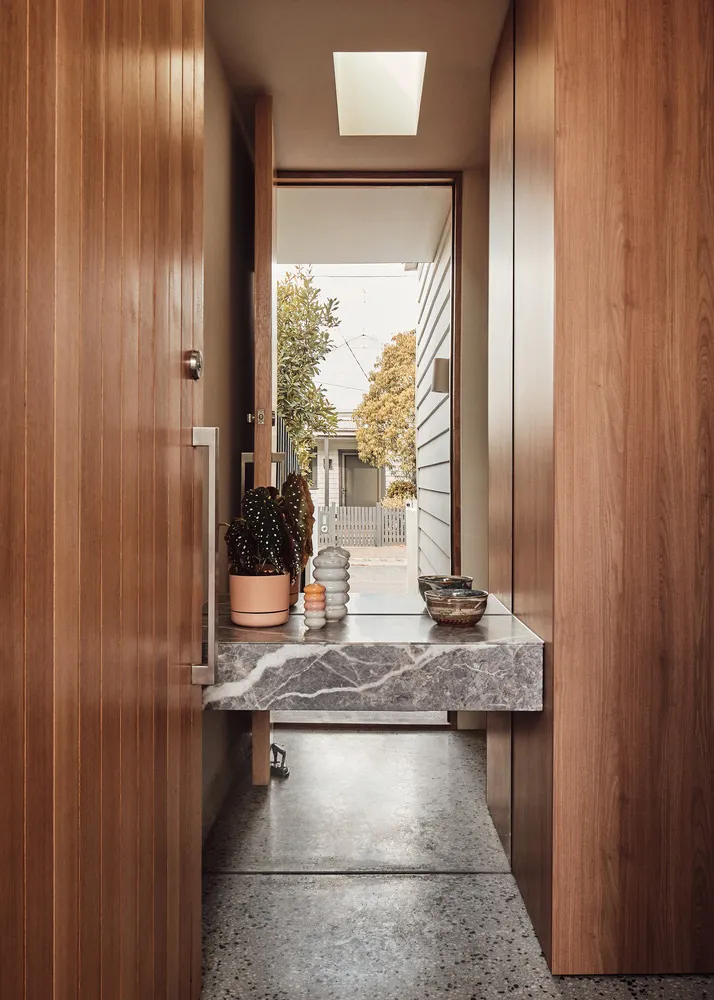 A minimalist entryway featuring a marble floor, wooden walls, and a small table with decorative items.