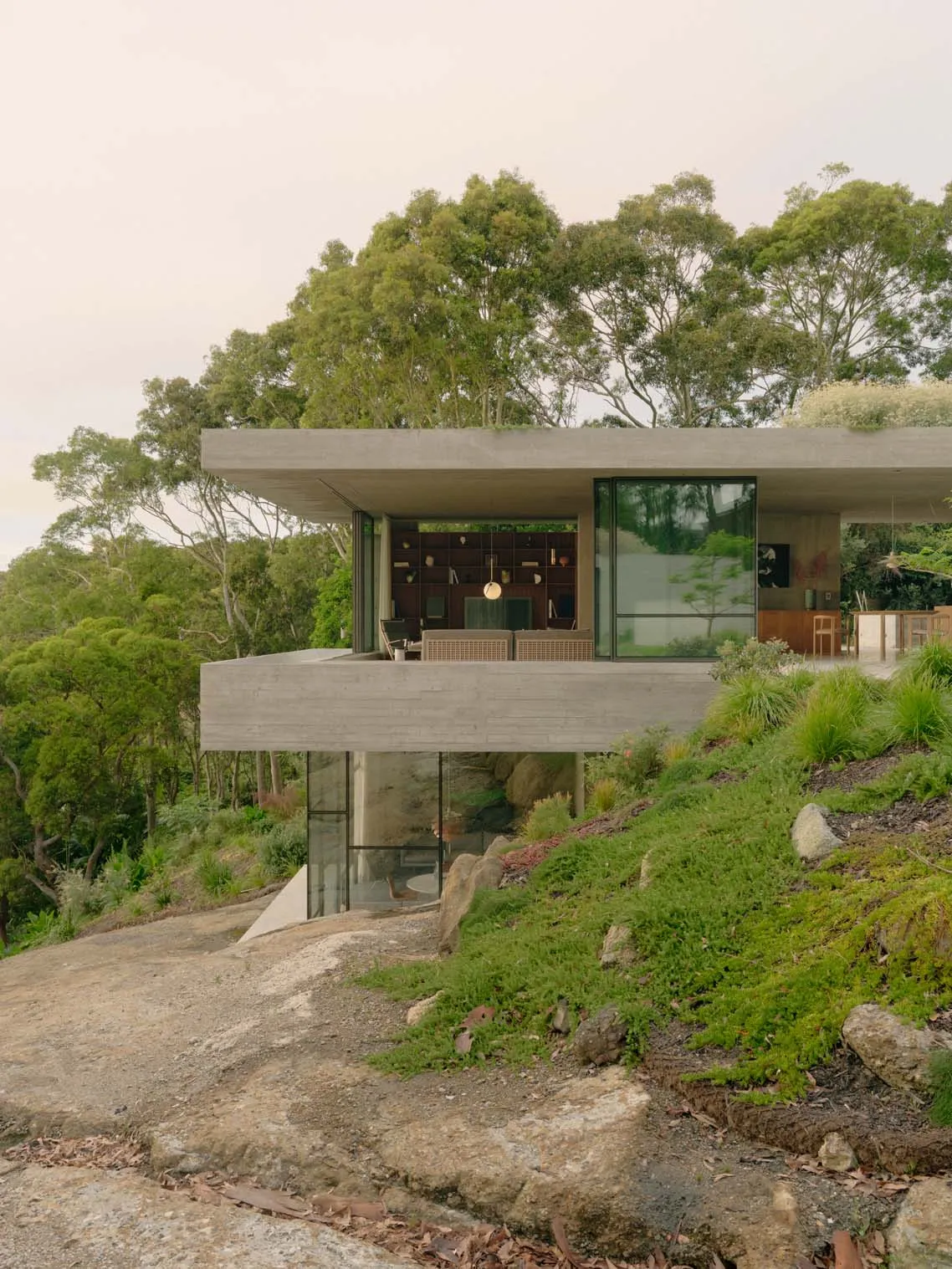 一座融入山坡的現代極簡小屋，擁有混凝土外牆與大面窗戶。