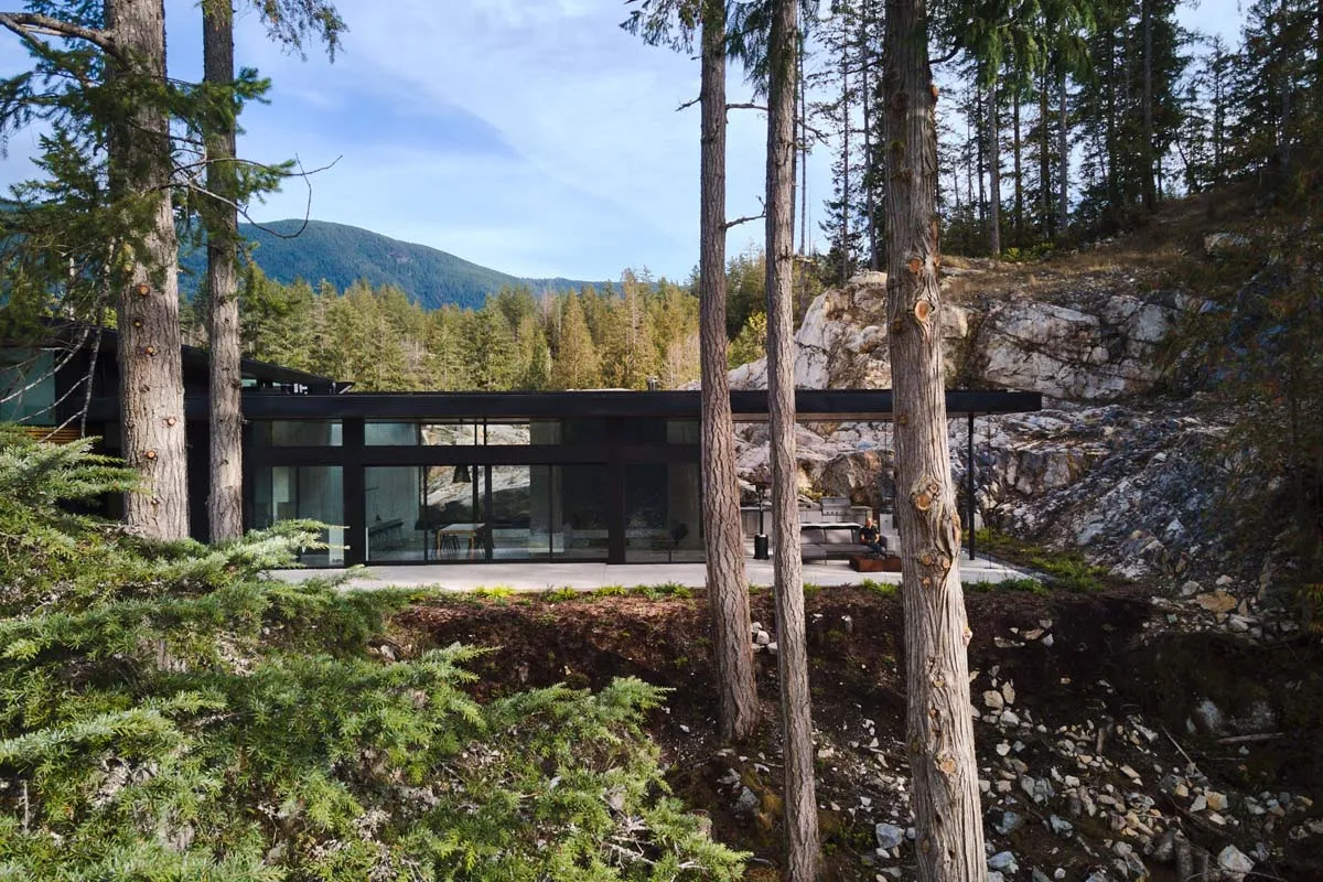 Modern residential home with large glass windows and concrete exterior nestled in a forested area.