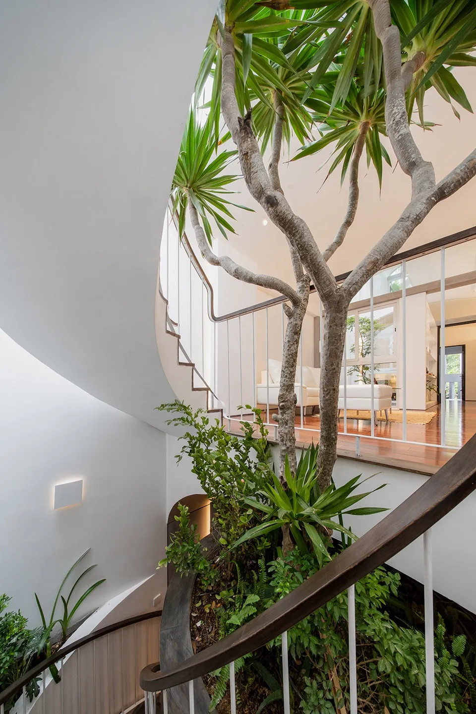 Modern staircase with greenery, wooden railings, and glass wall, featuring potted plants and natural light.