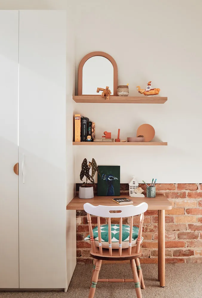 A minimalist home office setup featuring a wooden desk, a white chair, and a brick wall backdrop.
