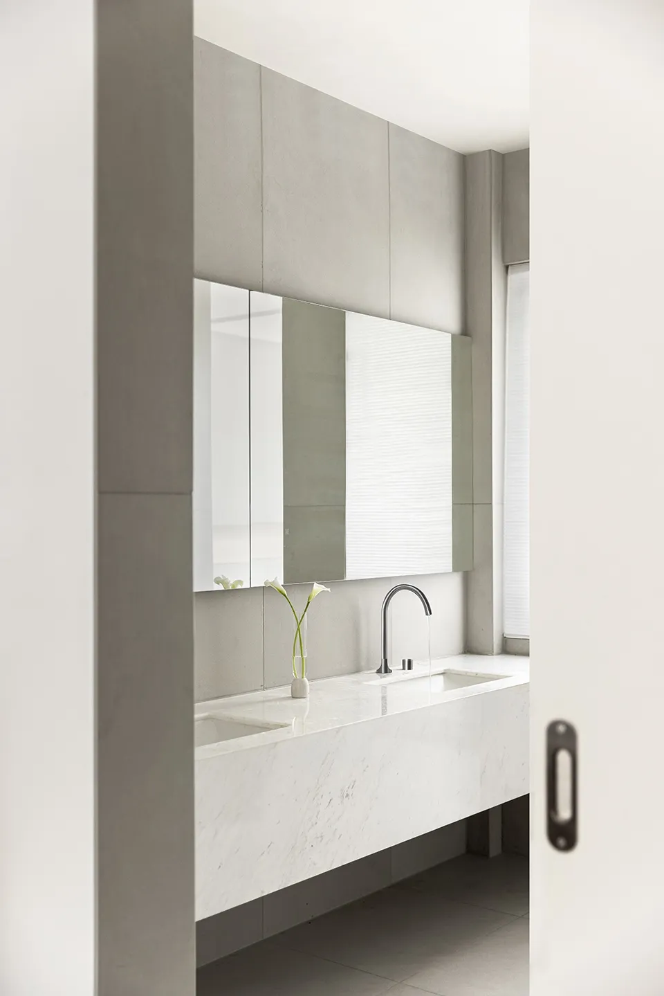 A minimalist bathroom featuring a white marble sink and countertop, with a large mirror and sleek faucet.