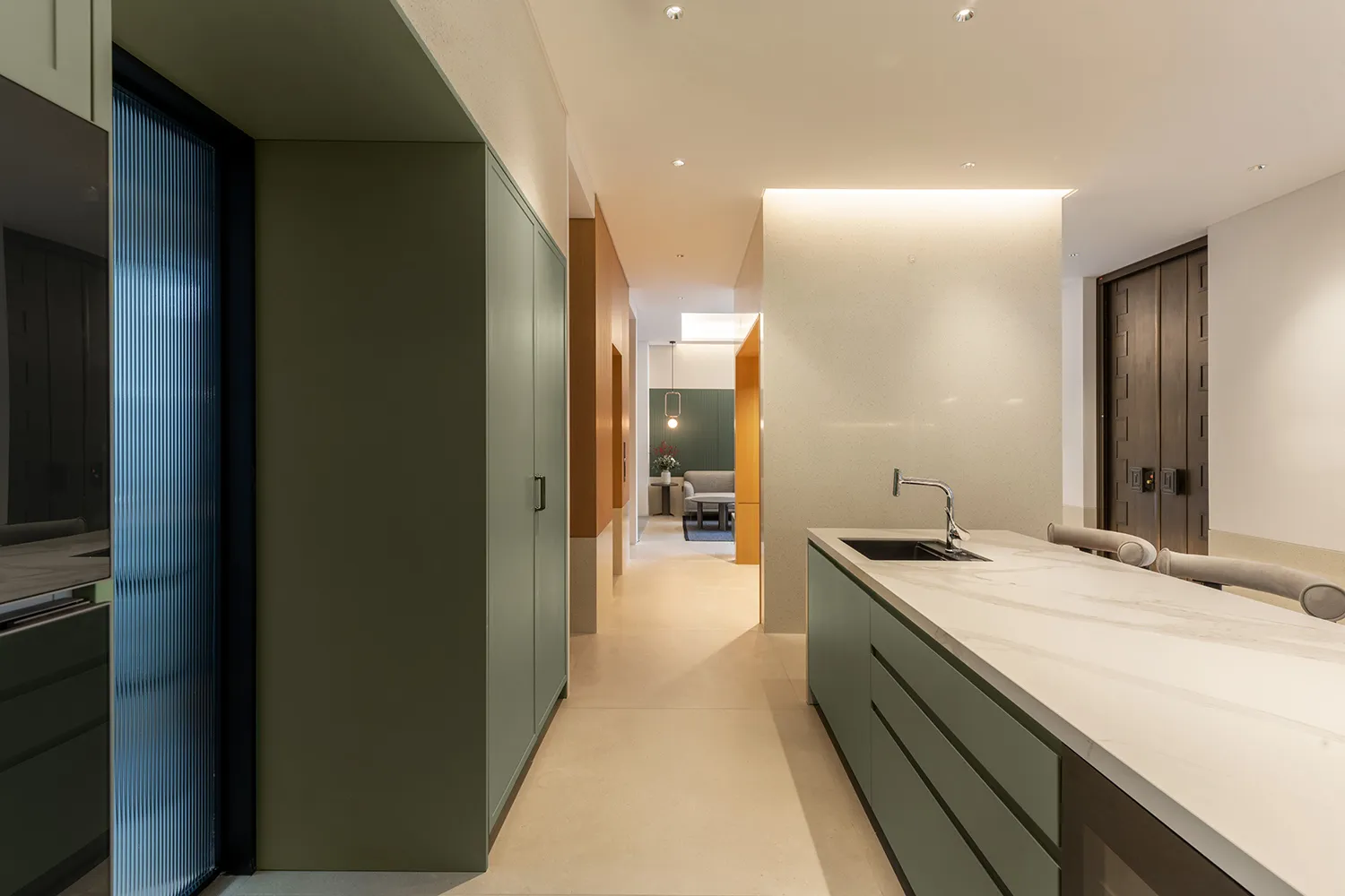 A modern residential interior with green kitchen cabinetry and marble countertops.
