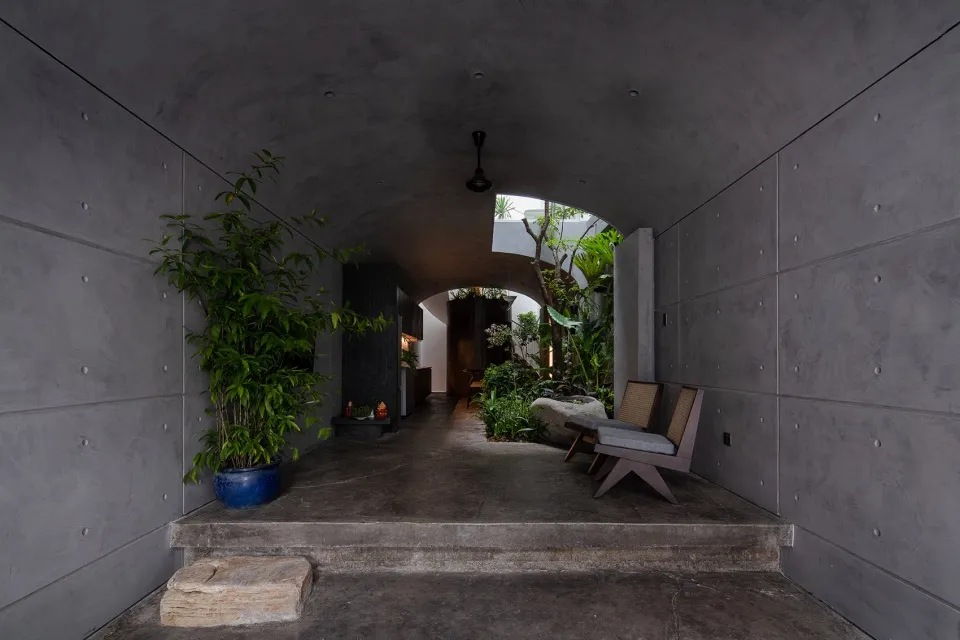 A minimalist entrance with concrete walls and a natural stone step leading to a greenery-filled courtyard.
