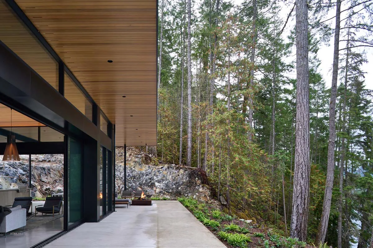 Modern residential exterior featuring wood, concrete, and stone materials in a forest setting.