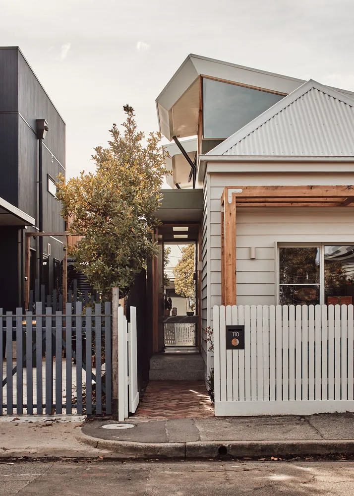 Modern house with wooden and metallic accents, featuring a white picket fence and a corrugated metal roof.