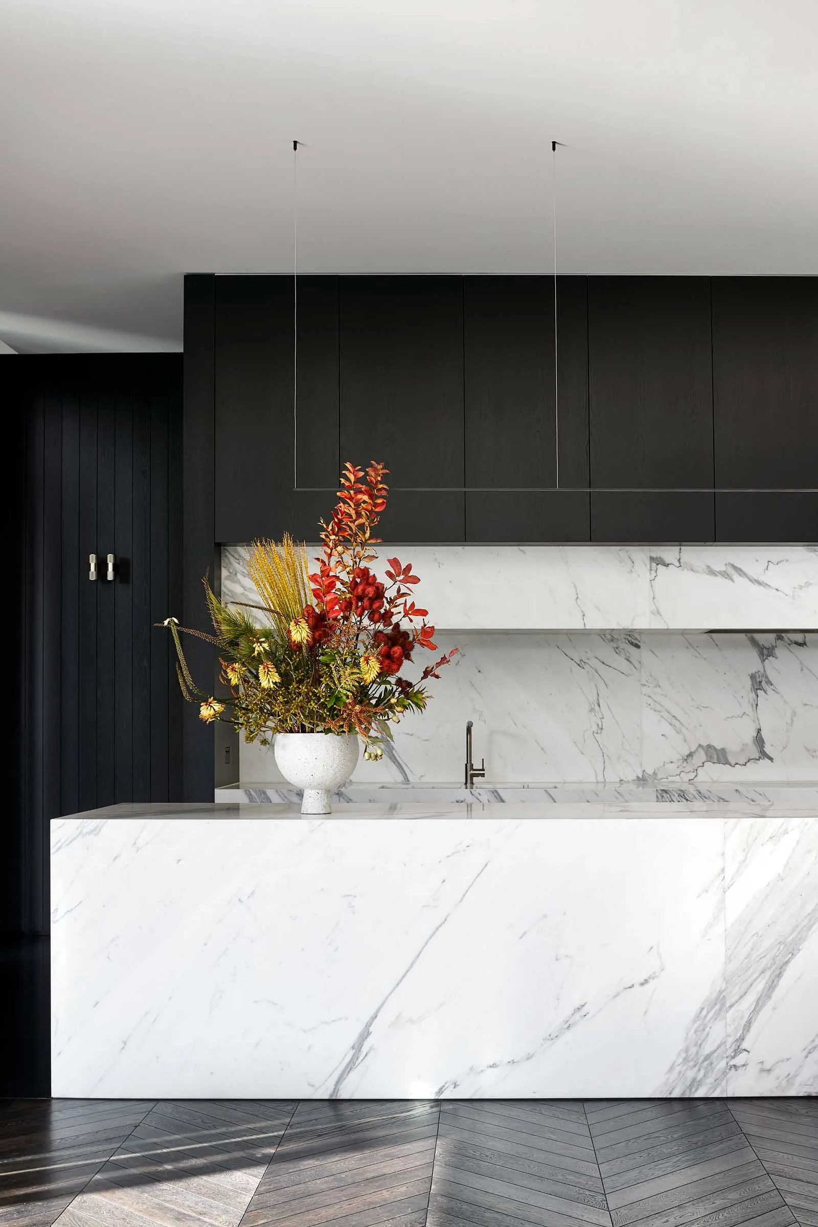 A modern kitchen with a large marble island featuring a vase of flowers and black cabinets.