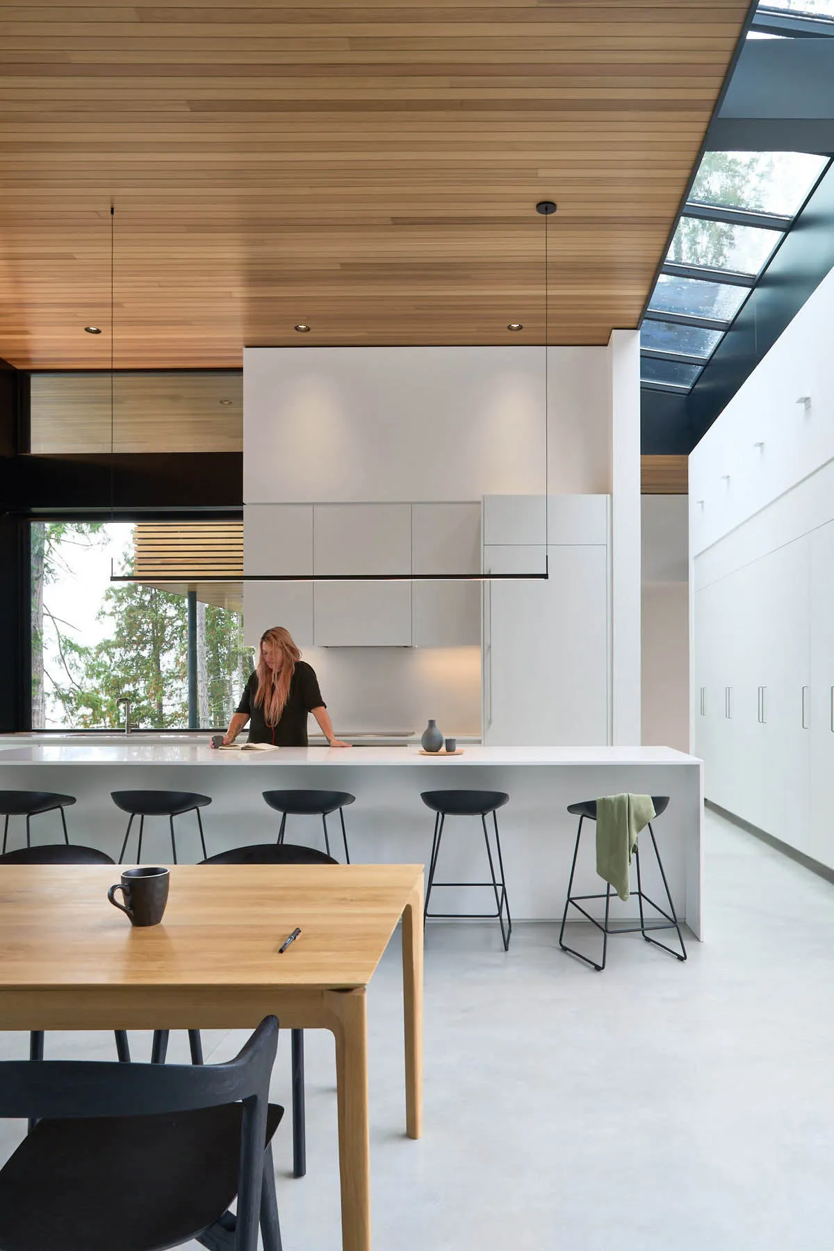 A modern kitchen with white painted cabinets, black stools, and a large skylight.