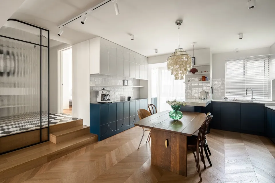 Modern minimalist kitchen with wooden flooring, glass cabinetry, and metal accents.