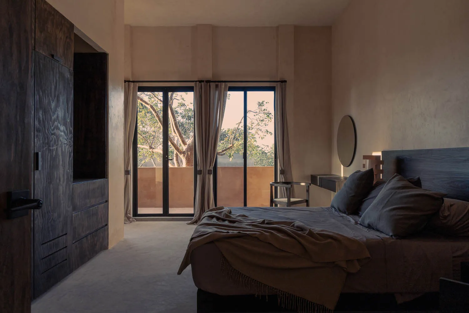 A minimalist bedroom with textured cement walls and a large window overlooking a balcony.
