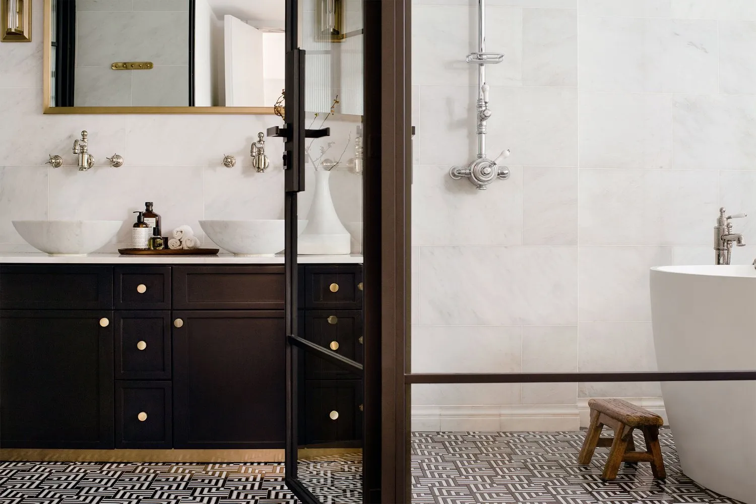 A modern residential bathroom featuring a white marble floor, white marble walls, and a black vanity with white sinks.