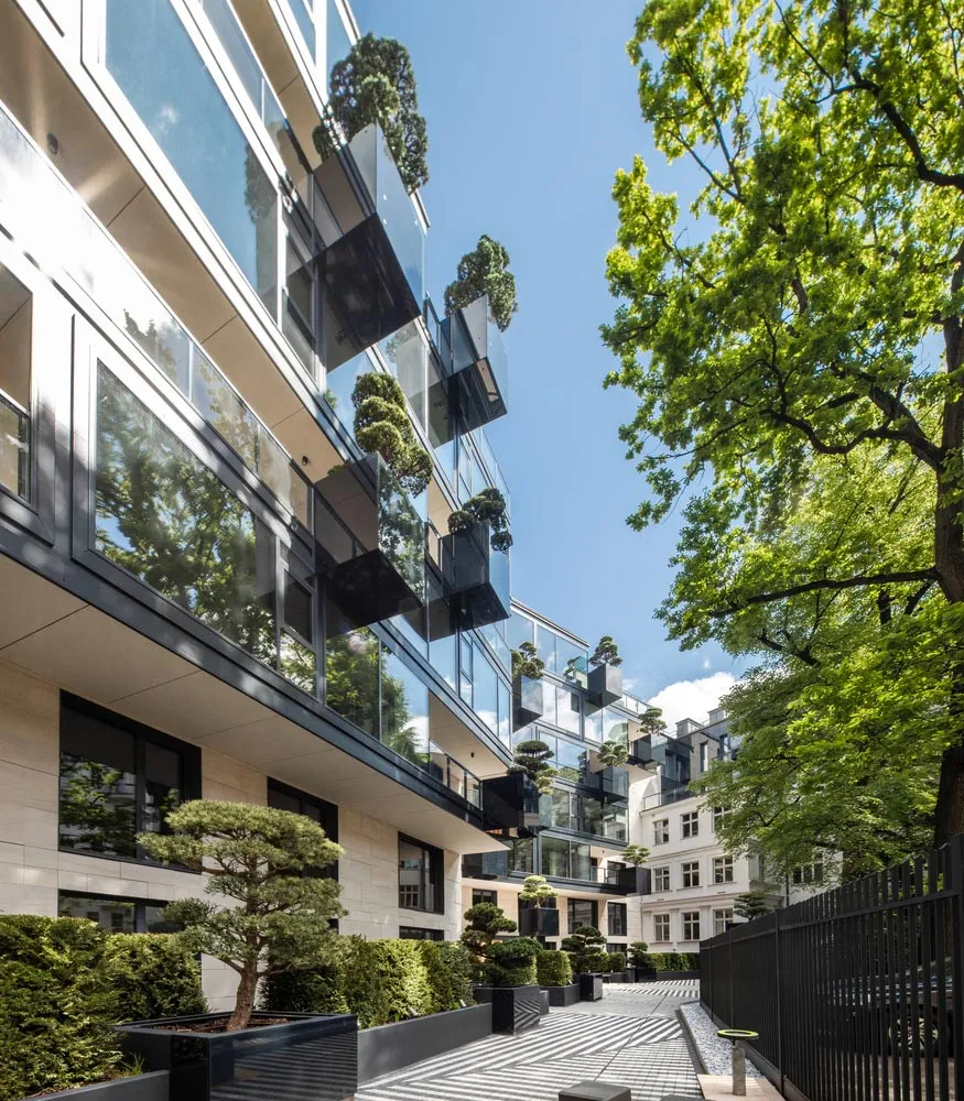 A modern residential building with glass walls and greenery on balconies.