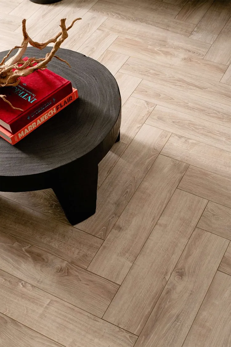 A modern indoor setting featuring a dark, round, wood-texture-tile coffee table with a red book and driftwood decoration.