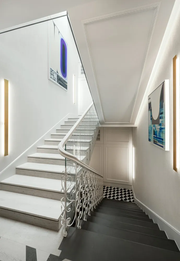 Modern interior staircase with concrete steps, white walls, and a black and white checkered floor. Features abstract art on t