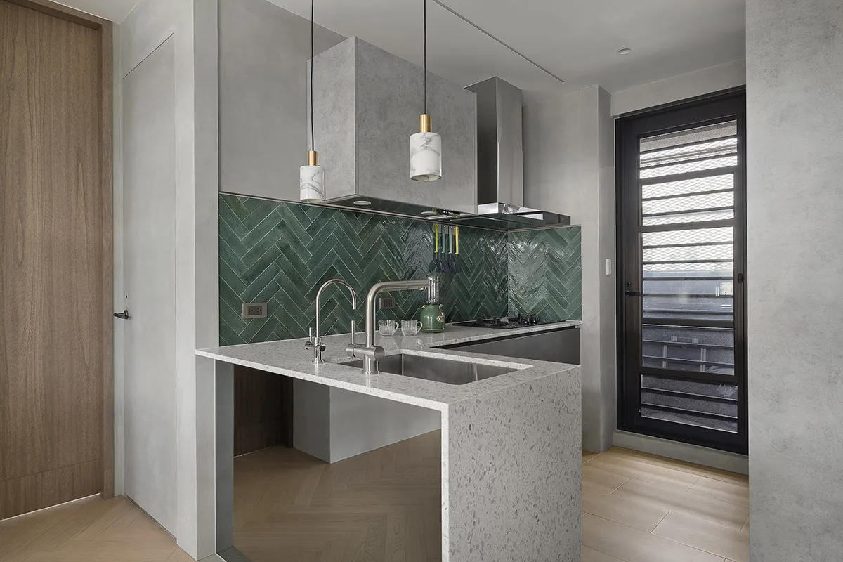 Modern kitchen featuring terrazzo countertops and green herringbone backsplash tiles.