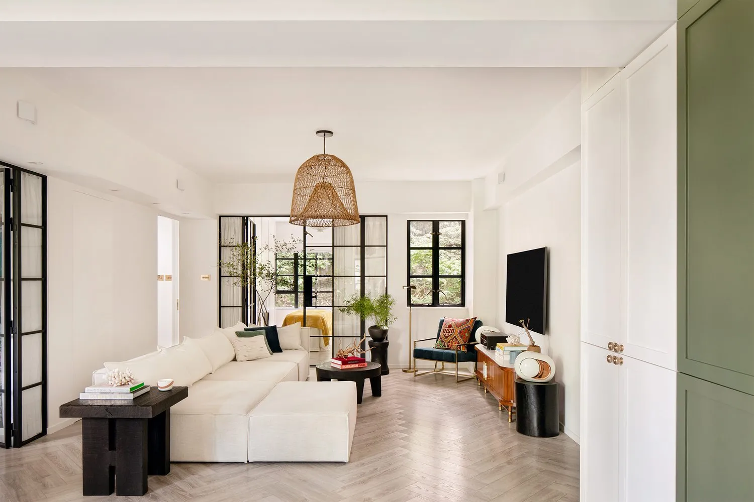 Modern living room featuring a white sectional sofa, woven pendant light, and green cabinets.