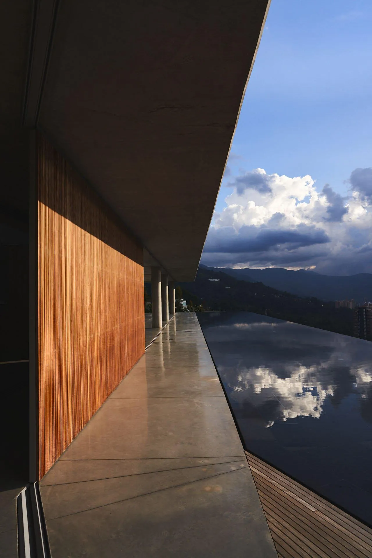 Modern residential exterior featuring a sleek, concrete balcony overlooking mountains and clouds.