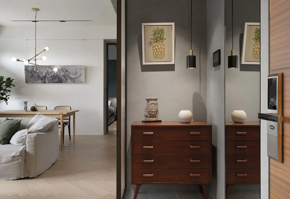 A modern minimalist living room with a grey sofa, wooden chest of drawers, and pineapple artwork on the wall.