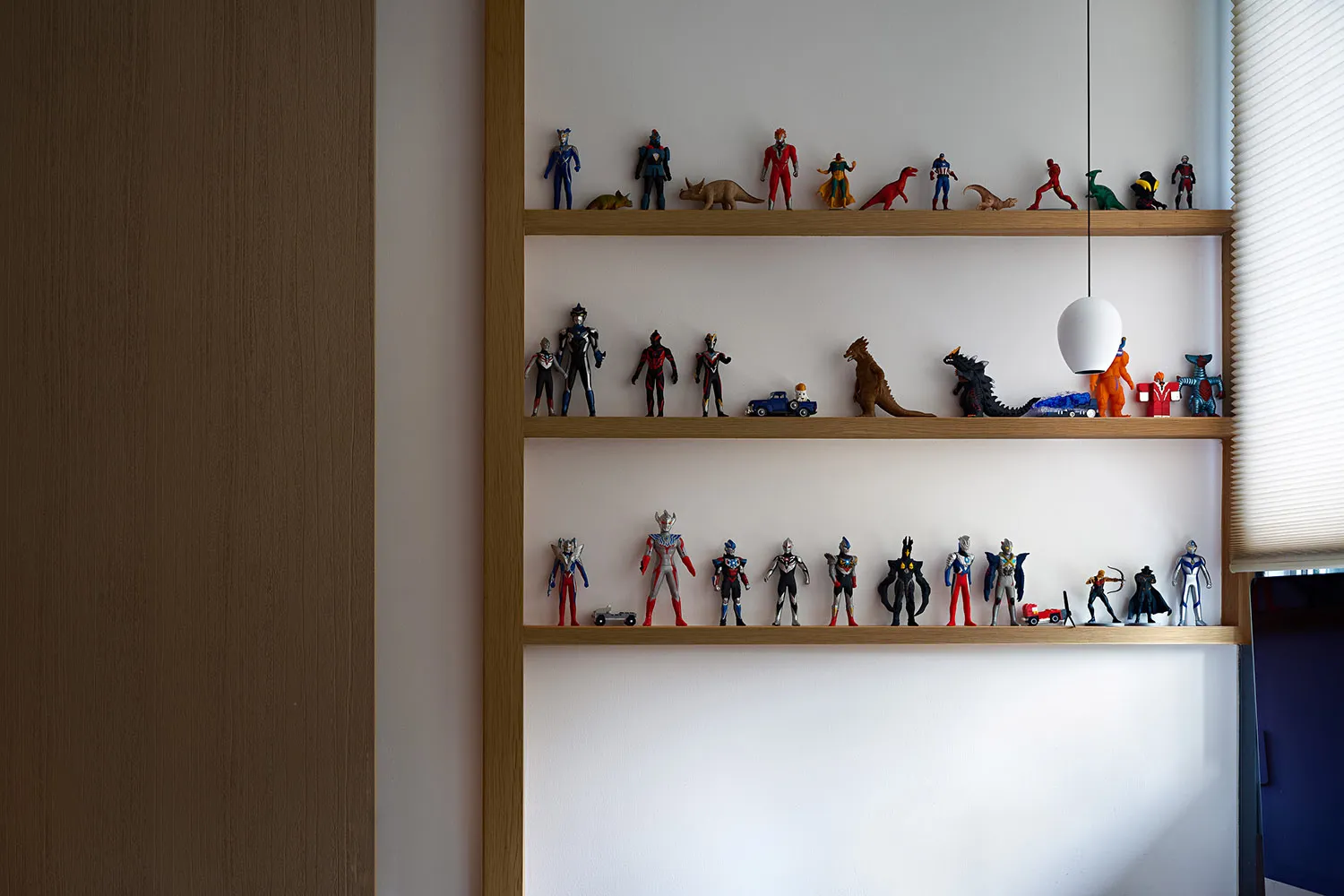 A wooden shelf with various toy figurines and dinosaur models arranged neatly on white walls.
