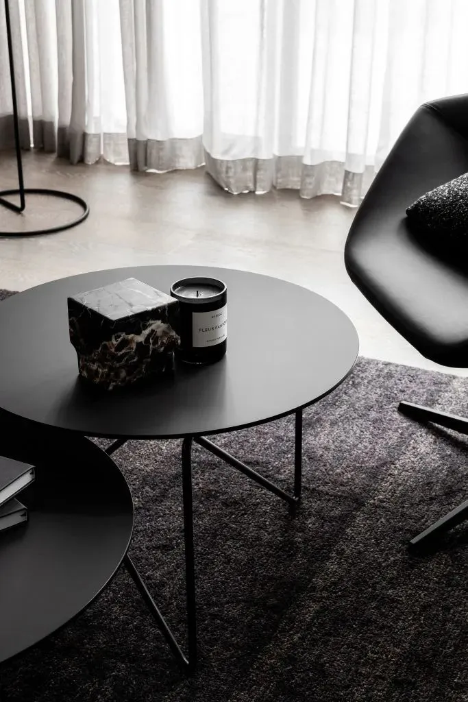 A modern, black metal side table with a candle, sculpture, and stack of books on it.
