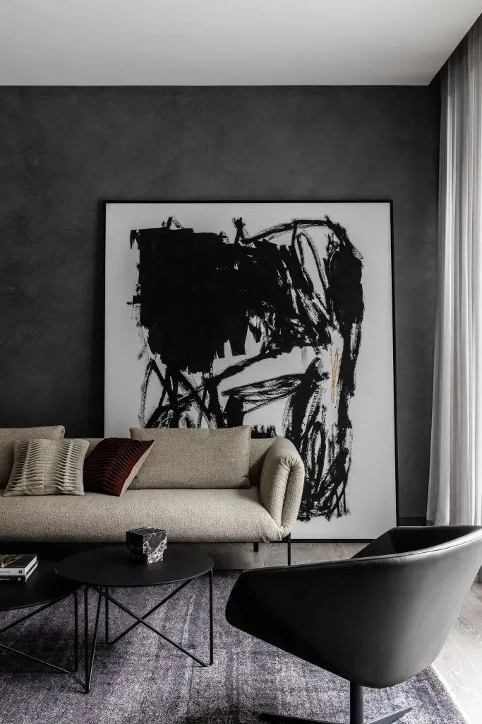 A modern living room featuring a beige sofa with decorative pillows, black tables, and a large black and white abstract paint