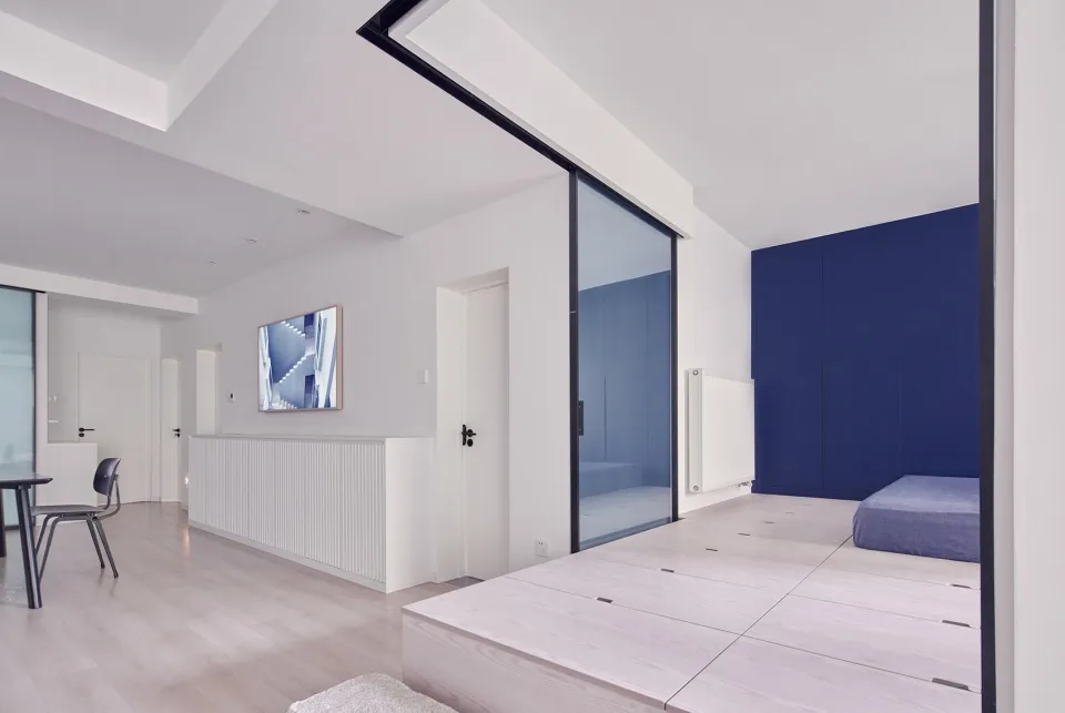 Modern minimalist living space with white walls and wooden floor, featuring a sliding glass door and blue storage compartment