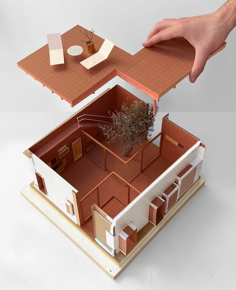 A model of a house made from paper and cardboard, with a tree inside and a hand lifting a section of the building.