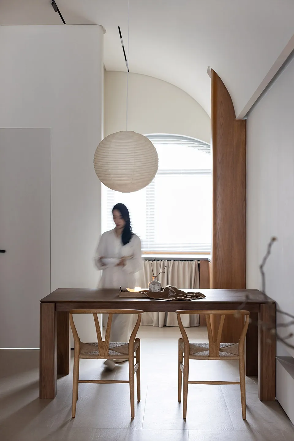A modern living room featuring a wooden table, chairs, and pendant light, with a minimalist design and natural wood elements.