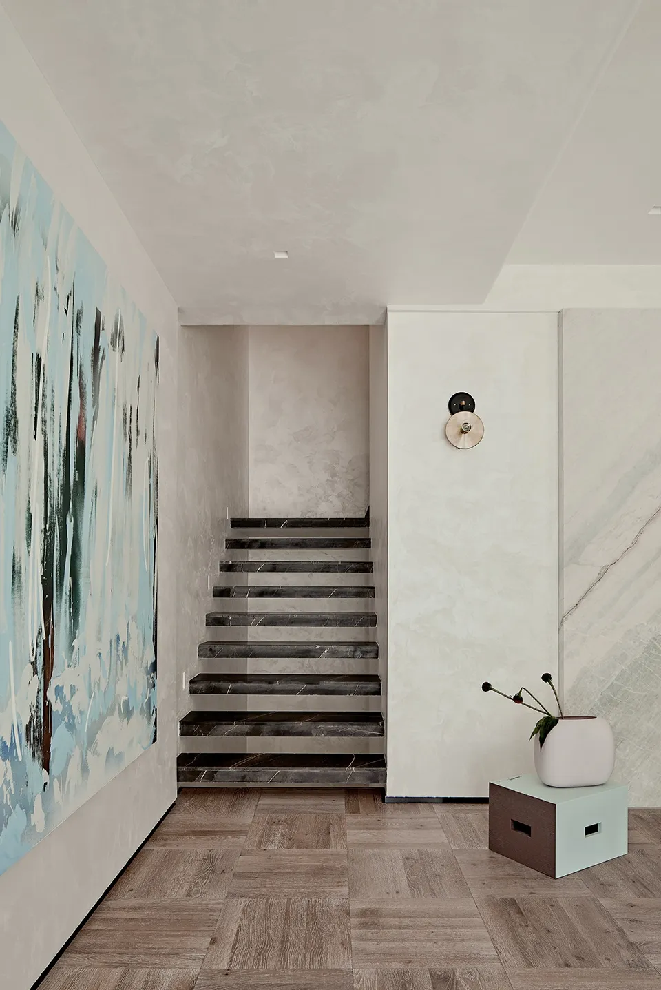 A modern staircase with black marble steps against a light-colored wall and a wooden floor. A large abstract painting hangs o