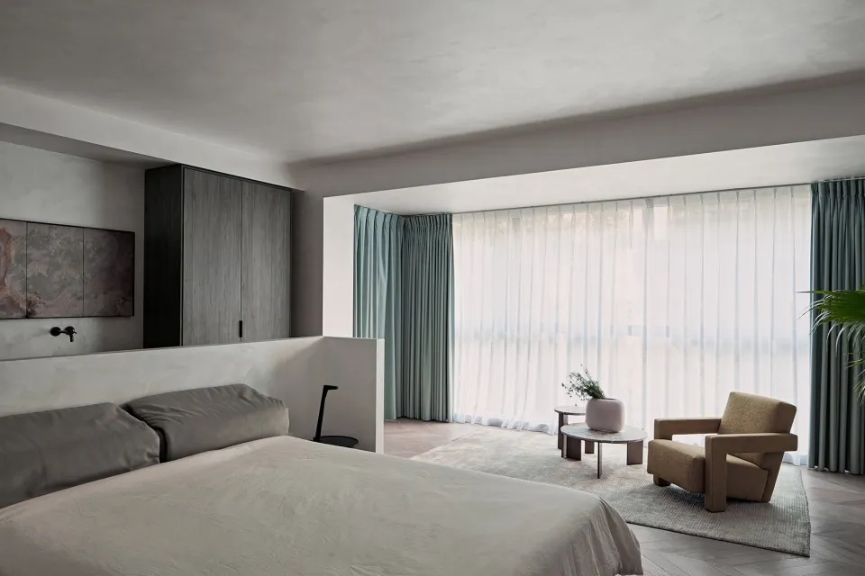 Minimalist bedroom with textured finishes, large window, and comfortable seating area.