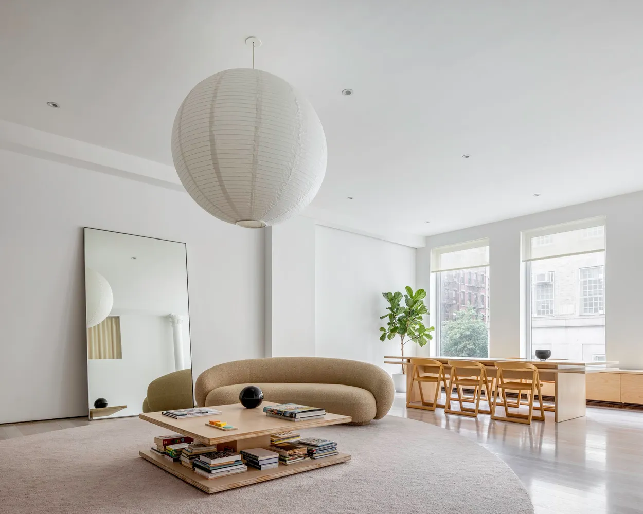 A modern, minimalist living room with a neutral color palette, featuring a curved sofa, wooden coffee table, and large floor