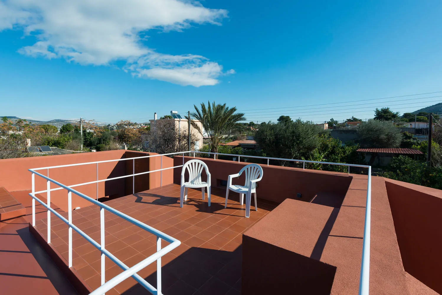 Modern rooftop patio with concrete flooring and white chairs.