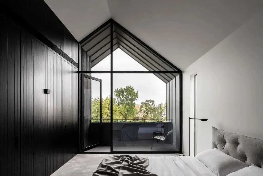 A modern bedroom with a black wall, a large window with a view of trees, and a bed with a textured headboard and blanket.