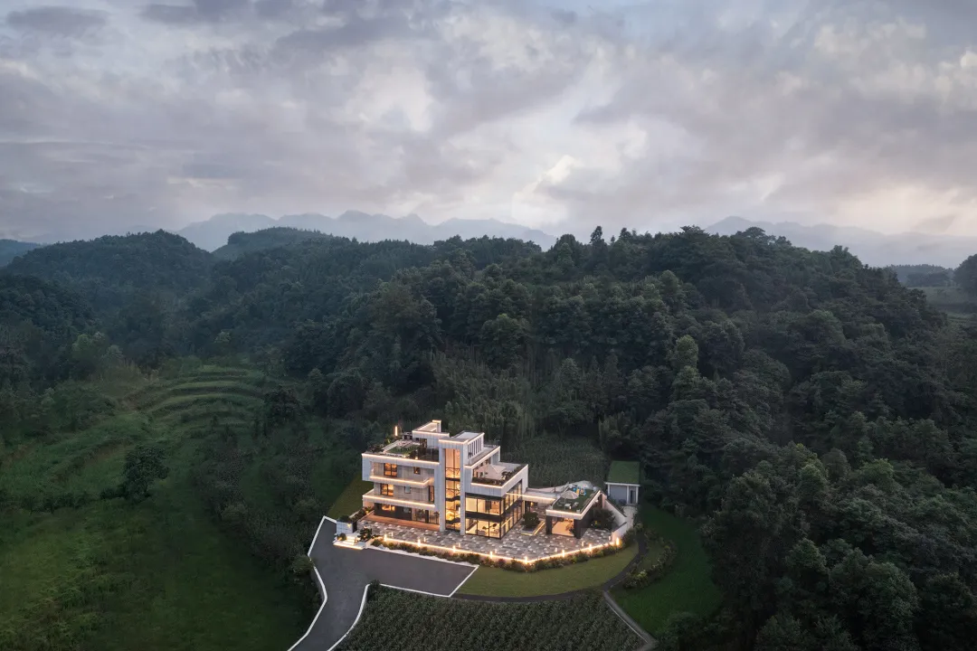 A modernist house with glass and concrete exteriors surrounded by lush greenery and mountains in the background.