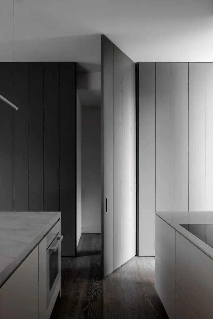 A modern minimalist kitchen with white marble countertops and dark wooden flooring.