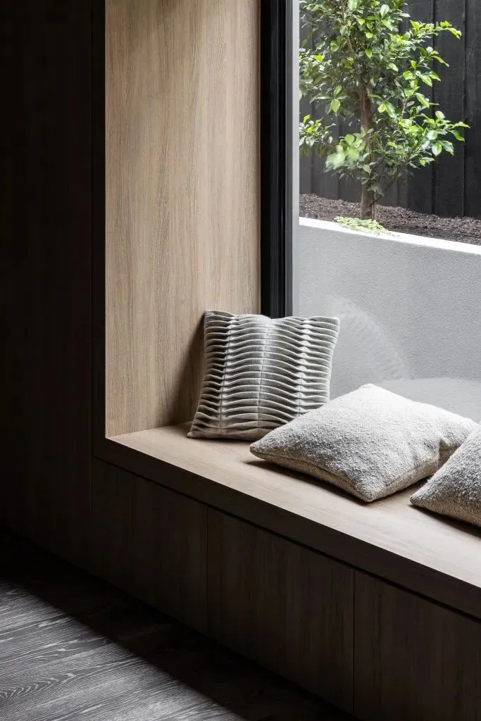 A modern window seat with wooden seating and cushions.