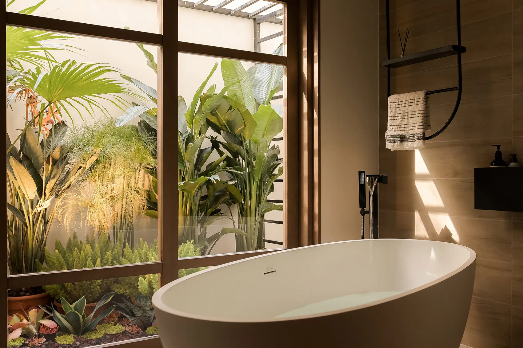 A minimalist bathroom featuring a freestanding bathtub with a serene indoor garden visible through the large window, providin