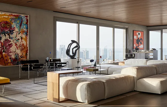 A contemporary living room featuring a concrete floor, large windows, white sectional sofa, and colorful abstract art.