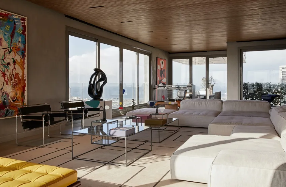 A modern concrete living room with large windows and a comfortable seating area, featuring a sleek coffee table and abstract