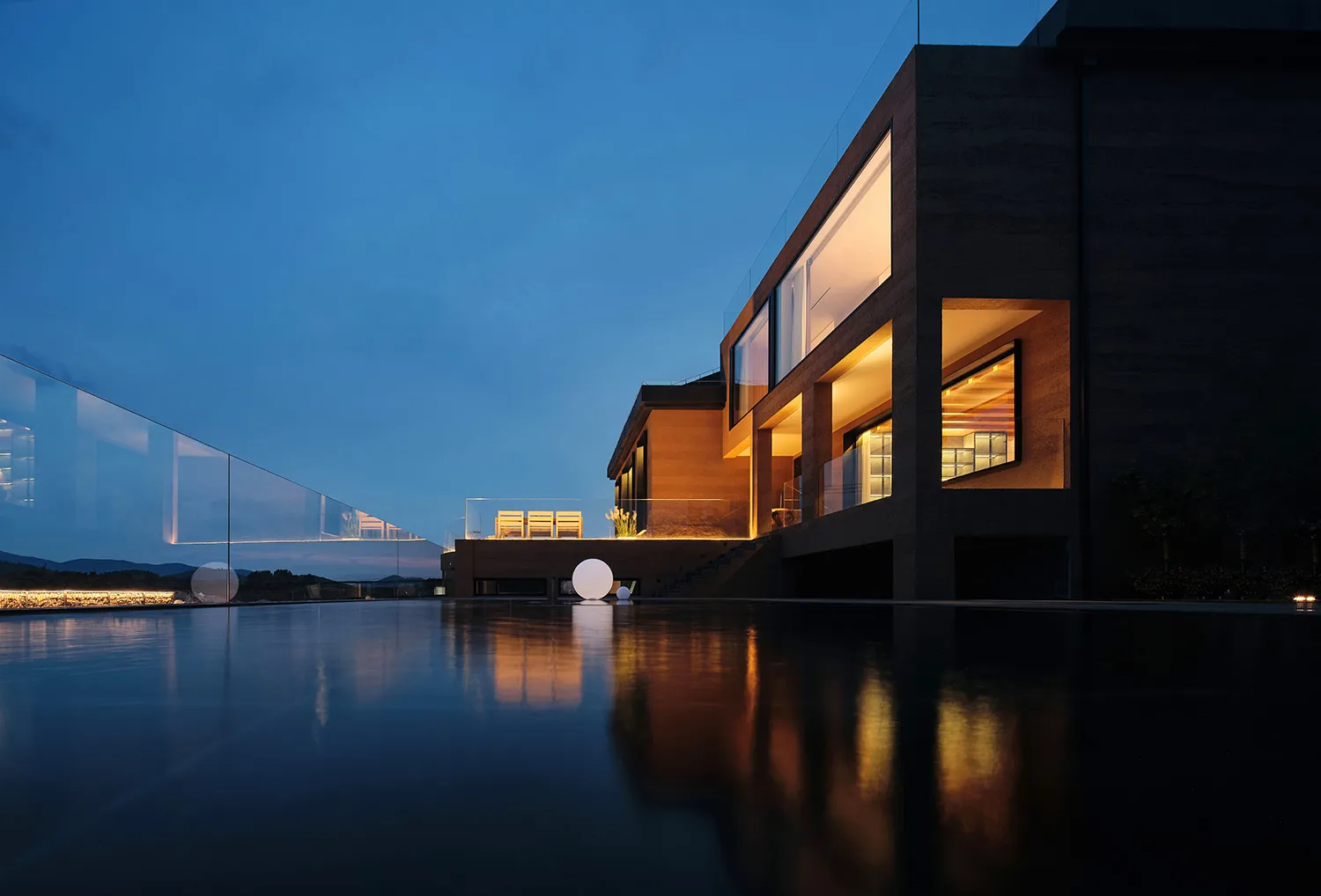 Modern residential exterior with large glass windows and illuminated interior.